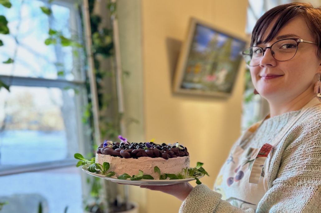 Kuvassa hymyilevä silmälasipäinen nainen, joka kannattelee täytekakkua.
