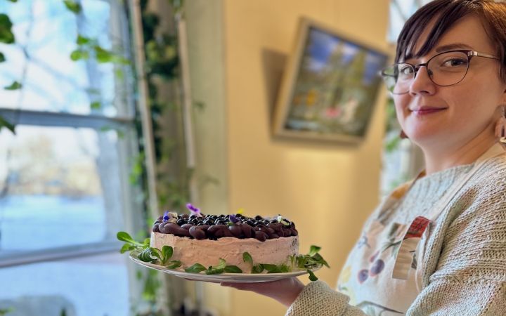 Kuvassa hymyilevä silmälasipäinen nainen, joka kannattelee täytekakkua.