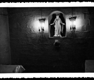 Hyvin pimeä kuva siunauskappelin sisältä. Seinällä olevassa syvennyksessä näkyy uskonnollinen patsas ja sen vierellä seinäkyntteliköt.