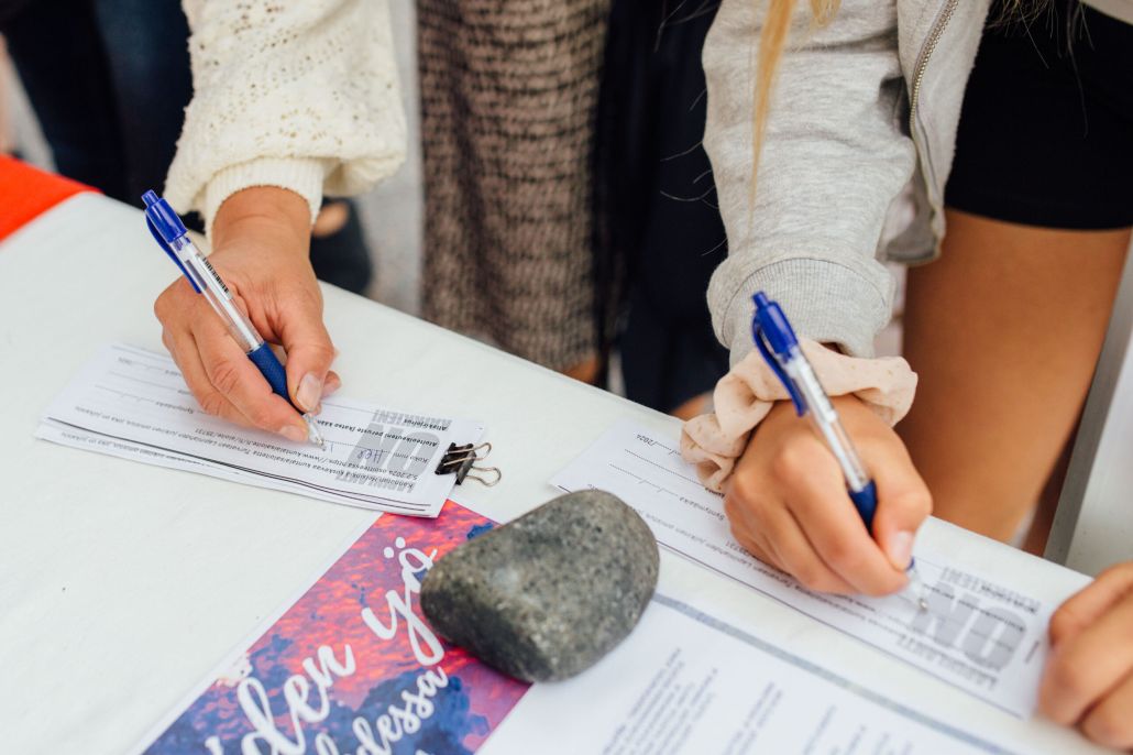 Lähikuva kahden henkilön käsistä allekirjoittamassa kuntalaisaloitelomaketta