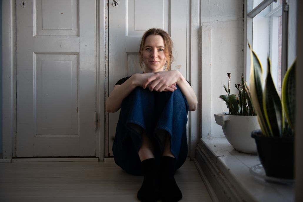 Kuvassa nuori naisoletettu istuu lattialla ja nojaa selällään puiseen oveen.