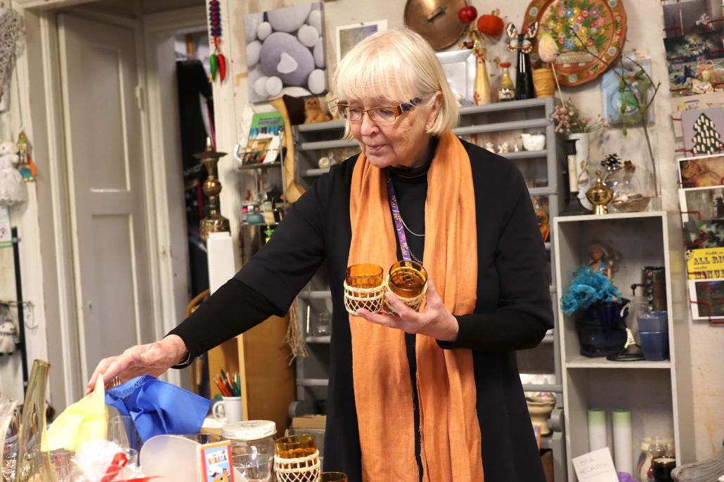 Kuvassa Piksi McArthur kirpputorilöytöjen äärellä, eli Lähteen Patinan pitkäaikainen vapaaehtoistyöntekijä.