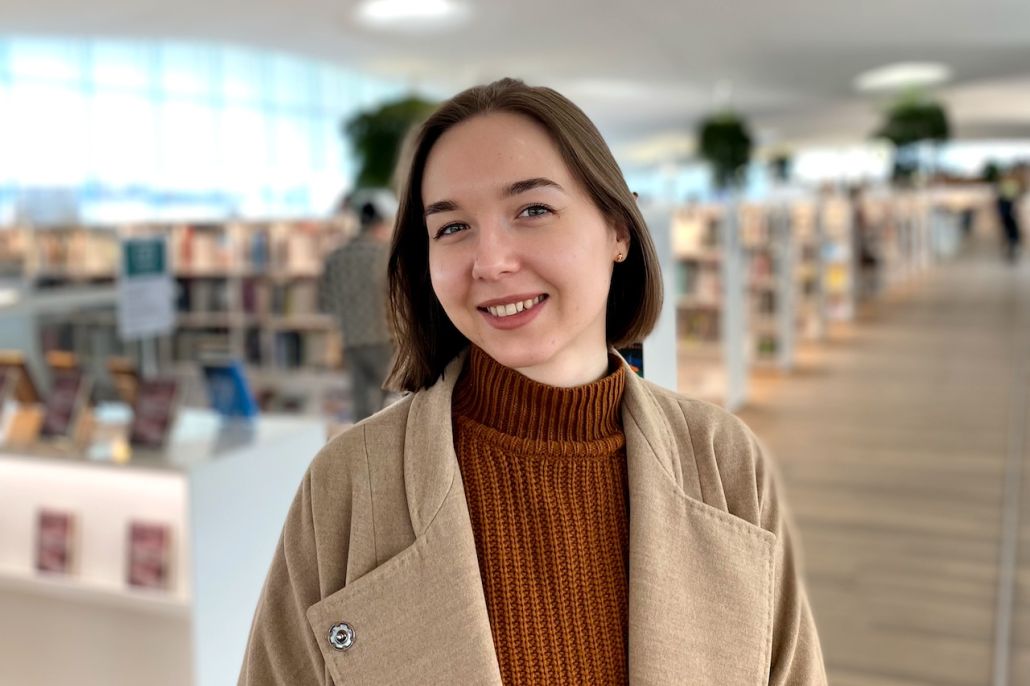 Kuvassa nainen kirjastossa, hymyilee kameralle