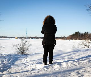 Nainen seisoo lumisessa maisemassa selkä kuvaajaan päin.