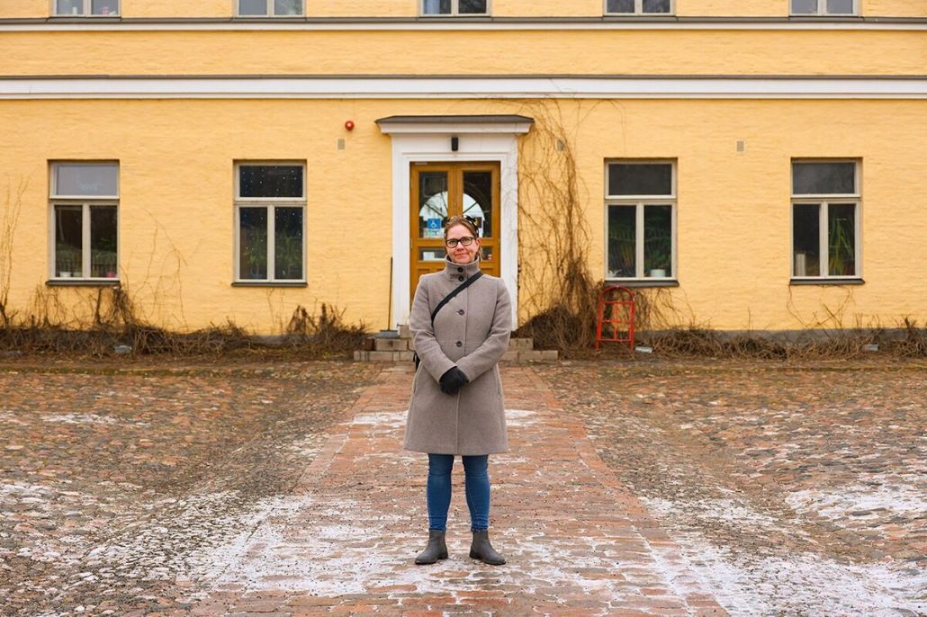 Kuvassa nainen seisoo Lapinlahden vanhan sairaalan edustalla huurteisella pihalla.