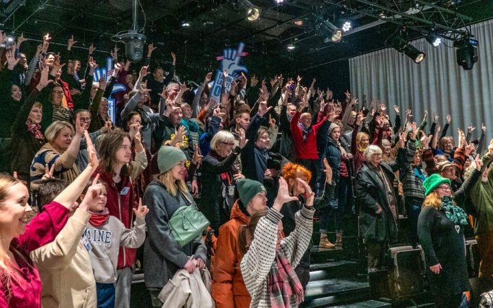 Kuvassa iso sali yleisöä kädet ilmassa kirjasto Oodin salissa.