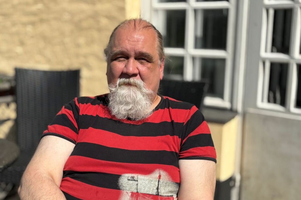 Parrakas mies istuu aurinkoisella parvekkeella.