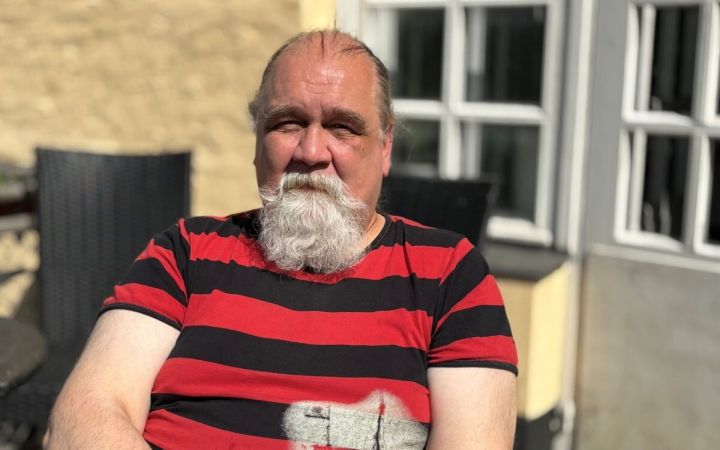 Parrakas mies istuu aurinkoisella parvekkeella.