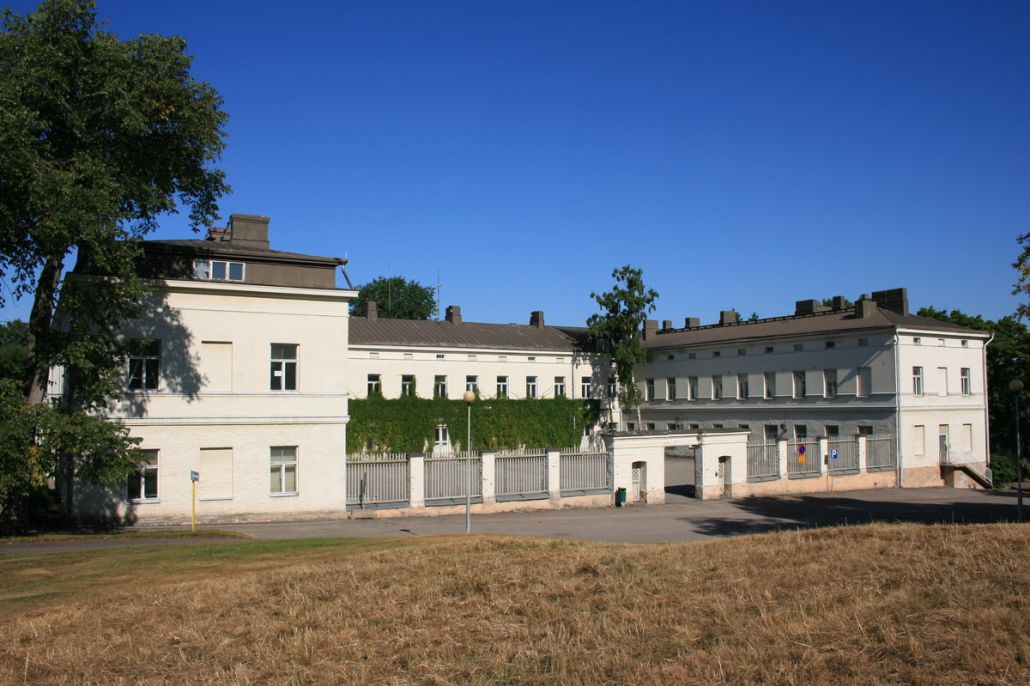 Lapinlahden sairaalarakennus kuvattuna etuviistosta. Etualalla kuivaa nurmikkoa ja taustalla sininen taivas.