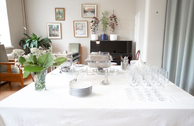 Kuvassa on katettu pöytä, jolla on lautasia, kukkamaljakko ja viinilaseja.