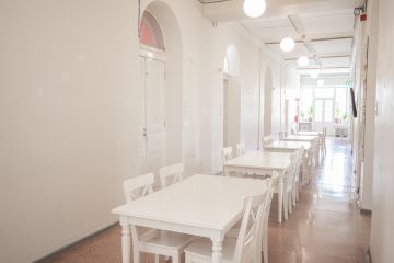 Kuvassa on Aleksis Kiven käytävä, jolla on pöytiä jonossa ja tuoleja.