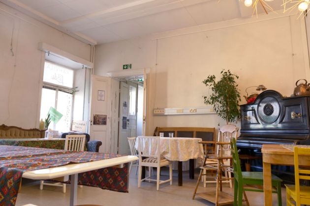 Kuvassa on Kahvila Lähteen ruokailutila, etualalla on pöytiä ja tuoleja ja taka-alalla piano.