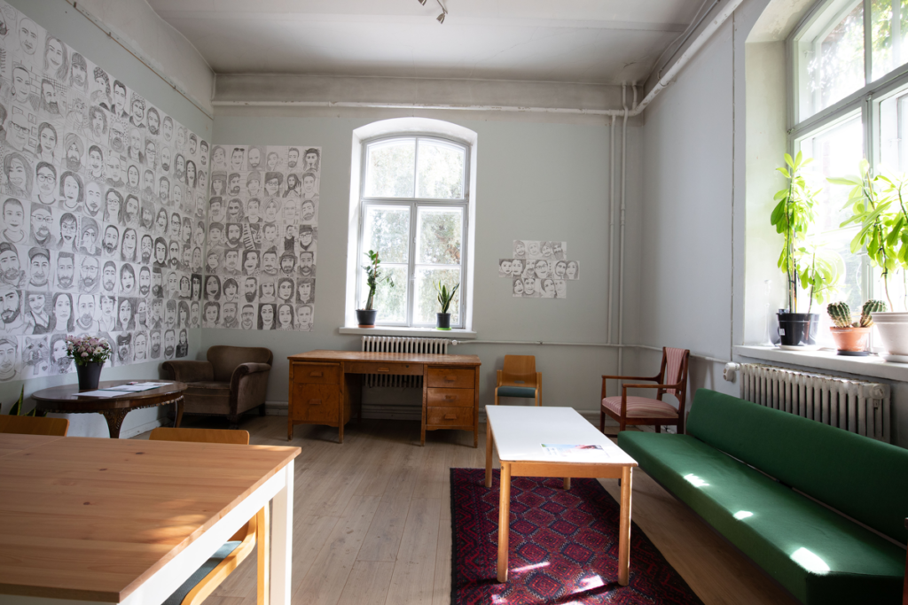 Kuvassa on Avoin tila sen ovelta kuvattuna, seinällä on taideteoksia ja etualla pöytiä ja sohvia.