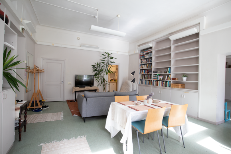 Kuvassa on Valo-tila, etualalla on pöytä ja tuoleja, taeempana sohva ja televisio. Oikealla on kirjahylly.