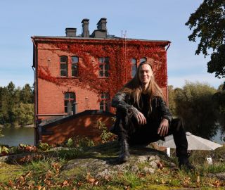 Tiilinen Venetsia-talo ja edustalla pitkähiuksinen istuva, hymyilevä mies.