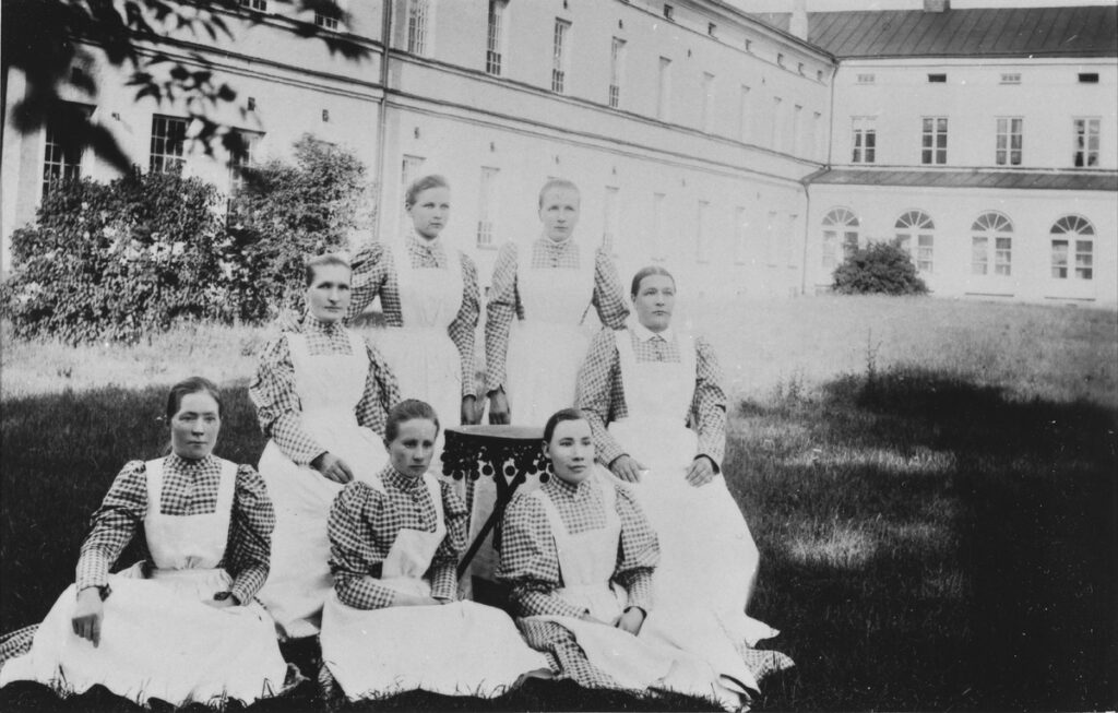 Mustavalkoisessa kuvassa valkoessuisia sairaanhoitajia poseeraamassa kameralle Lapinlahden sairaalan pihalla.
