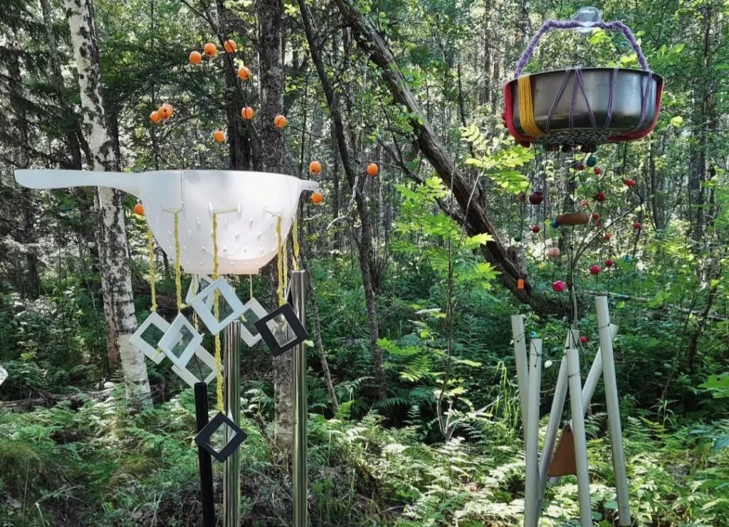 Metsässä erikoisia tuulikelloja, jotka on tehty muun muassa siivilöistä.