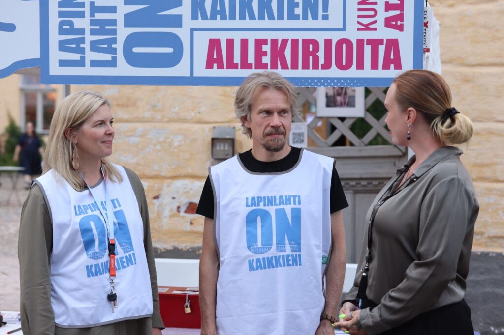 Kolme henkilöä keskustelee kuntalaisaloitteesta kampanjateltalla