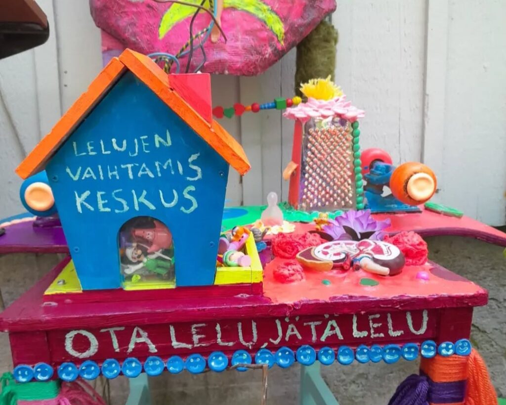 Värikkäitä leluja pöydällä ja teksti: Ota lelu tai jätä lelu
