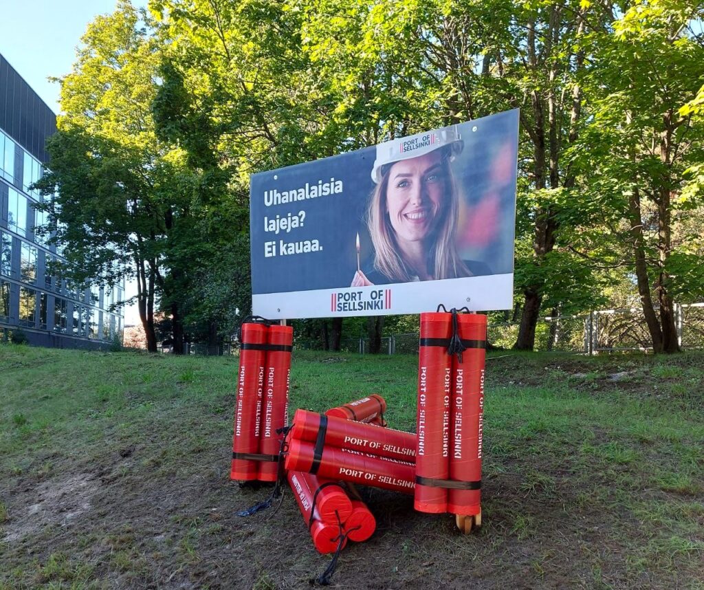 Satamatunnelia vastustava Port of Sellsinki -teos puistossa. Suuria dynamiitteja ja kyltti, jossa lukee "Uhanalaisia lajeja? Ei kauaa"