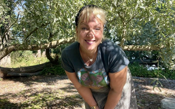 Vaalea nainen hymyilee puistossa puun katveessa.