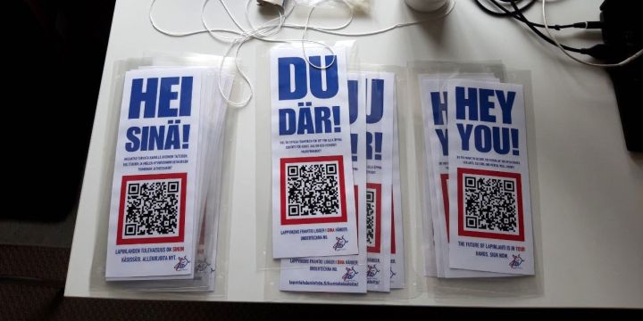 Laminoidut Hei sinä! -julisteet QR-koodilla valkoisella pöydällä