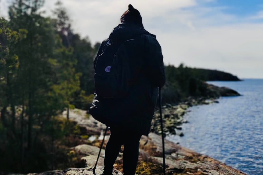 Nainen seisoo kalliolla, selin kameraan ja katsoo merelle.