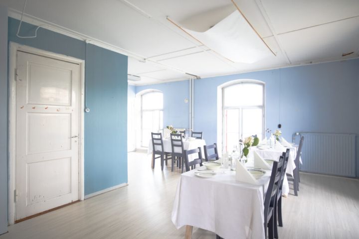 Kuvassa on katettuja pöytiä. Taaempana on ikkunoita, joista tulvii valoa huoneeseen. Vasemmalla on Sinisen huoneen ovi.