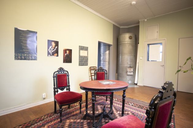 Kuvassa etualalla on pyöreä pöytä ja tuoleja. Taka-alalla on takka ja seinällä tauluja.