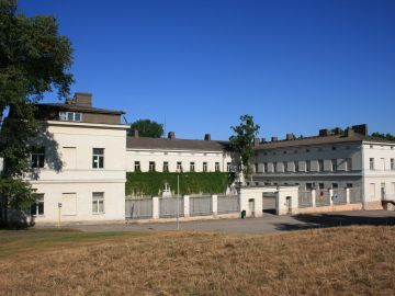 Lapinlahden sairaalarakennus kuvattuna etuviistosta. Etualalla kuivaa nurmikkoa ja taustalla sininen taivas.