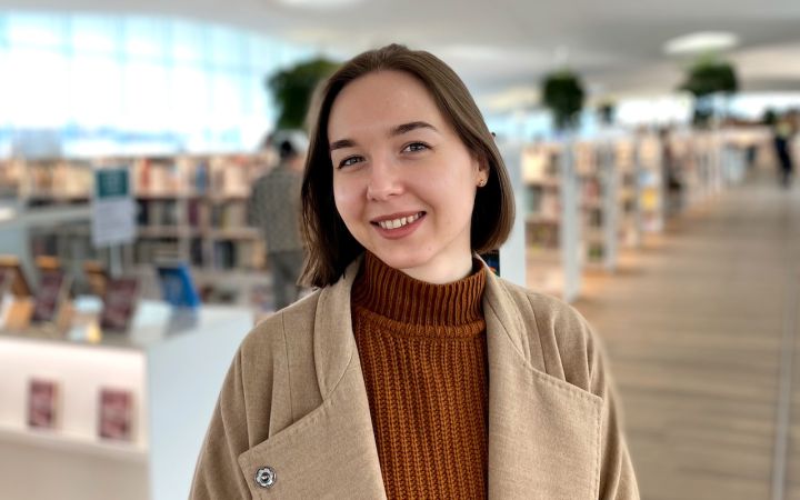 Kuvassa nainen kirjastossa, hymyilee kameralle