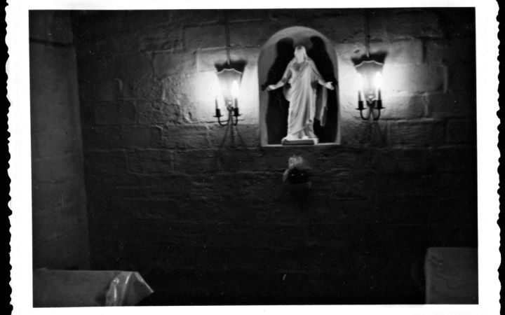 Hyvin pimeä kuva siunauskappelin sisältä. Seinällä olevassa syvennyksessä näkyy uskonnollinen patsas ja sen vierellä seinäkyntteliköt.