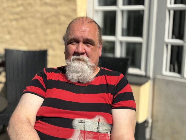 Parrakas mies istuu aurinkoisella parvekkeella.