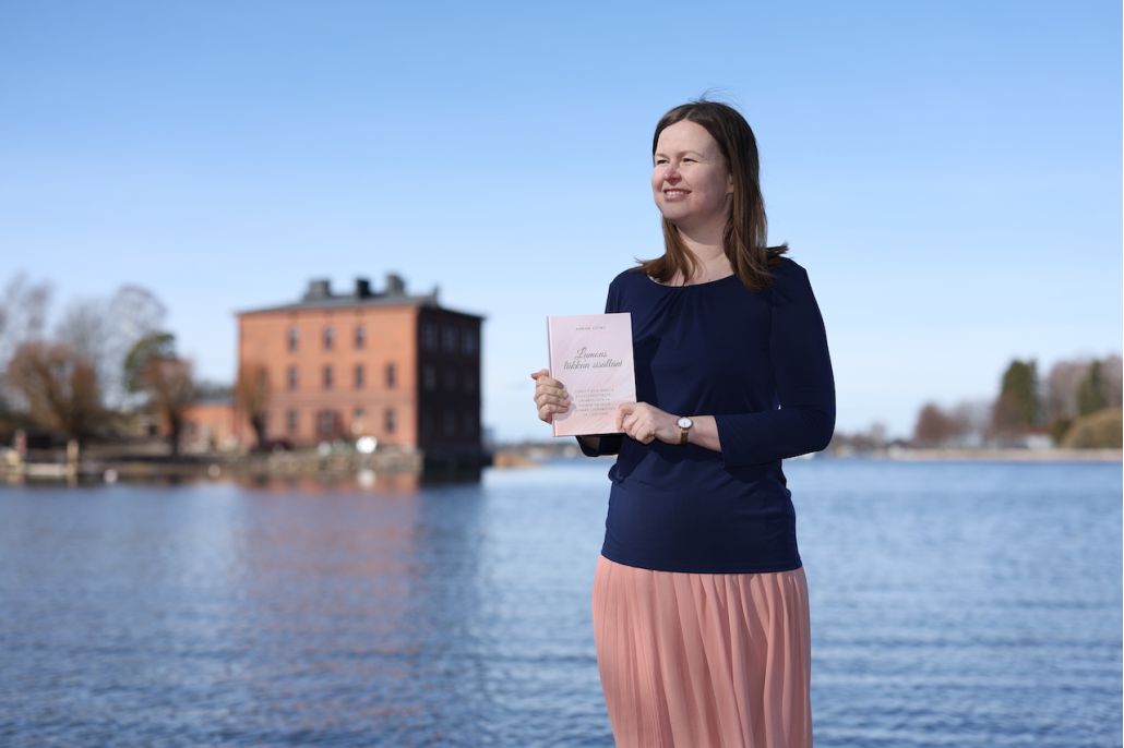 Kuvassa nainen Lapinlahdessa meren rannalla kirja sylissä, taustalla Venetsia-talo.