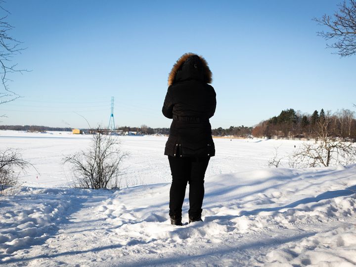 Nainen seisoo lumisessa maisemassa selkä kuvaajaan päin.