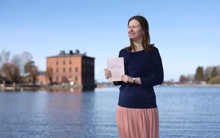 Kuvassa nainen Lapinlahdessa meren rannalla kirja sylissä, taustalla Venetsia-talo.