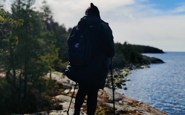 Nainen seisoo kalliolla, selin kameraan ja katsoo merelle.