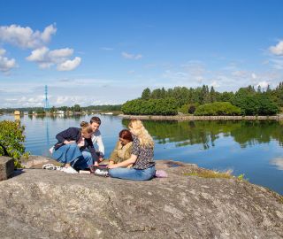 Neljä ihmistä aurinkoisilla Lapinlahden kallioilla meren äärellä keskustelemassa.