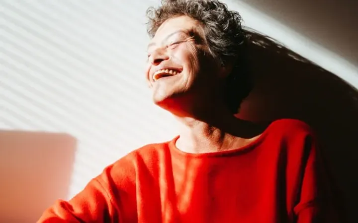 Punapaitainen vanhempi nainen nauraa auringossa.