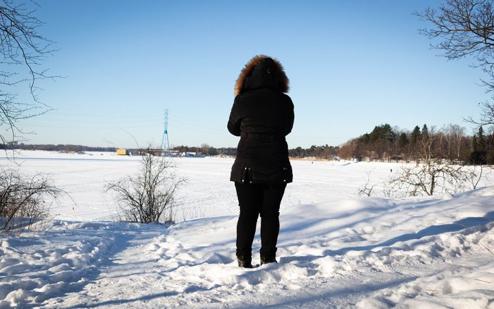 Nainen seisoo lumisessa maisemassa selkä kuvaajaan päin.