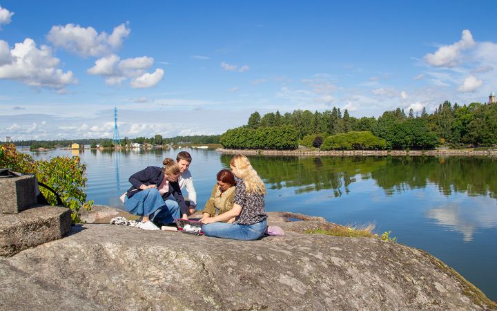Neljä ihmistä aurinkoisilla Lapinlahden kallioilla meren äärellä keskustelemassa.