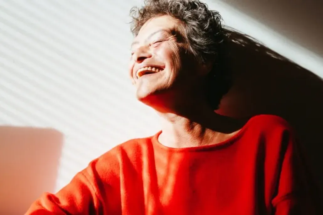 Punapaitainen vanhempi nainen nauraa auringossa.