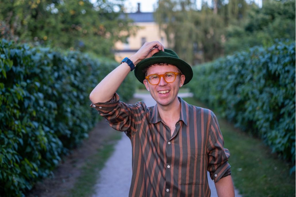 Kuvassa on hattupäinen, hymyilevä mies.