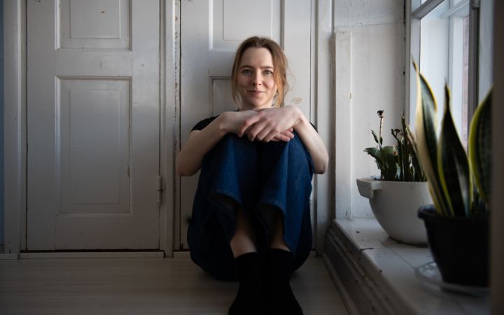 Kuvassa nuori naisoletettu istuu lattialla ja nojaa selällään puiseen oveen.