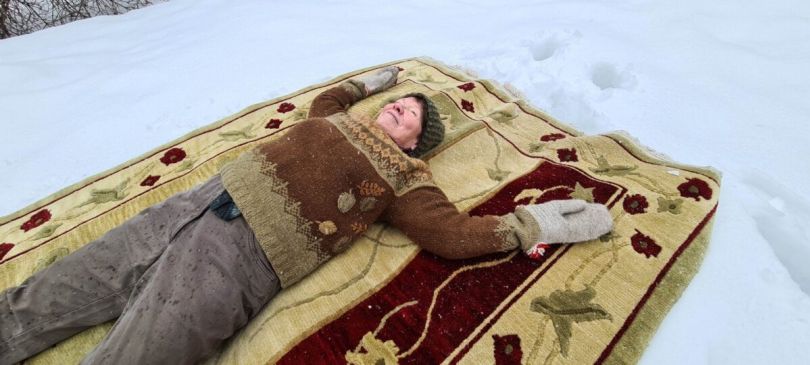 Nainen makaa maton päälle lumessa.