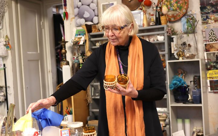 Kuvassa Piksi McArthur kirpputorilöytöjen äärellä, eli Lähteen Patinan pitkäaikainen vapaaehtoistyöntekijä.