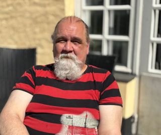 Parrakas mies istuu aurinkoisella parvekkeella.