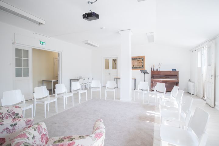 Kuvassa on tuoleja kehässä. Keskellä on matto ja taka-alalla piano.