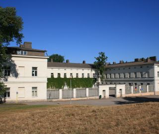 Lapinlahden sairaalarakennus kuvattuna etuviistosta. Etualalla kuivaa nurmikkoa ja taustalla sininen taivas.