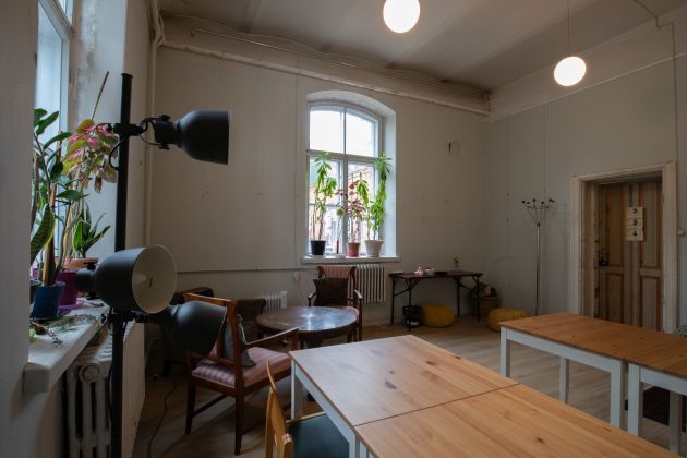 Kuvassa on Venetsia-talon Avoin tila nurkasta kuvattuna. Etualalla on pöytiä ja tuoleja, vasemmalla lamppuja.